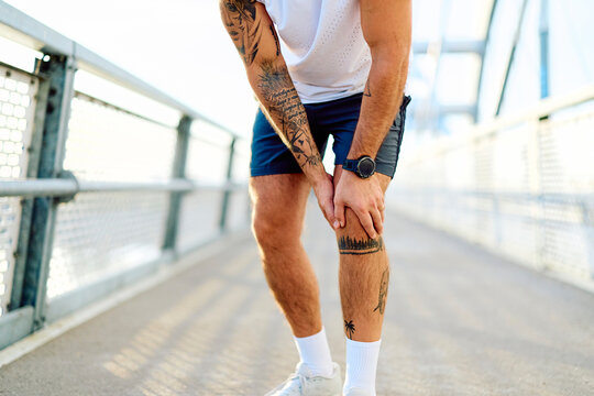 Athlete holding painful knee after running, symbolizing injury, joint pain, and healthcare needs during outdoor fitness