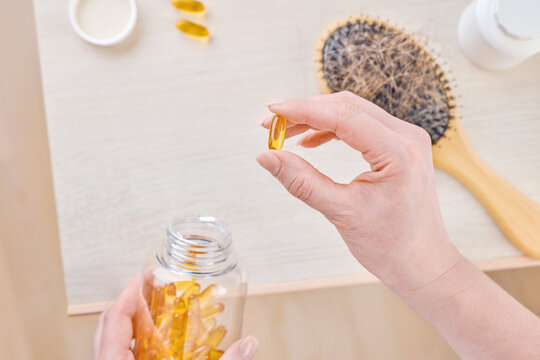 Hands hold a hair vitamin capsule beside a hairbrush full of shed hair