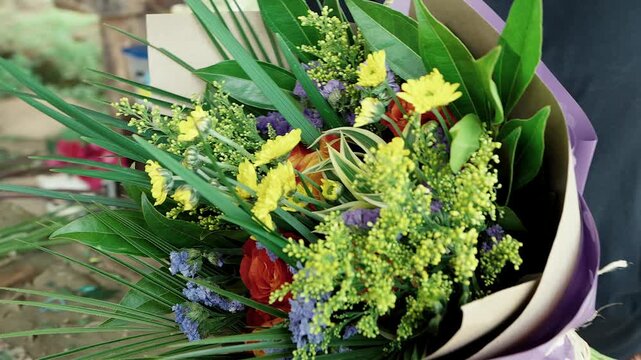 florist holding a completed colorful floral bouquet wrapped in paper