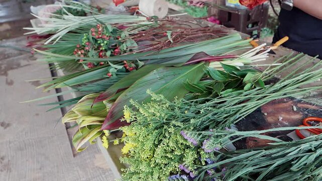 assortment of fresh flowers, tropical leaves, and berries laid out on a wooden table
