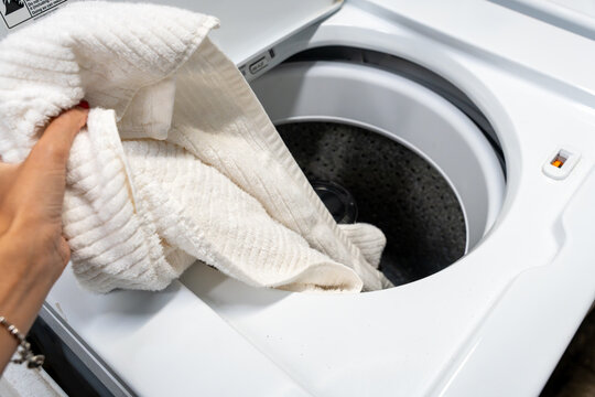 Hand loading laundry into a large top-loading washing machine, symbolizing sustainable living, water conservation and eco-friendly household technology