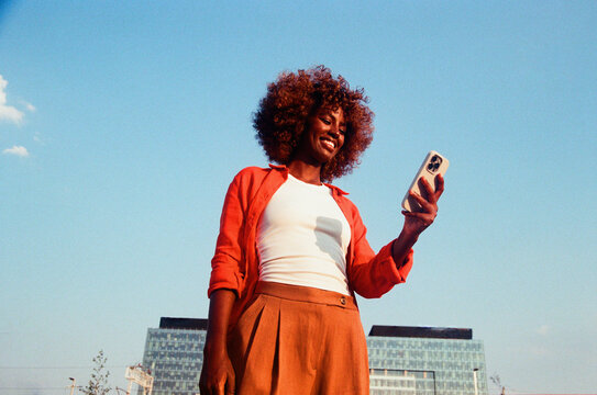 Woman checks smartphone in orange outfit film photo