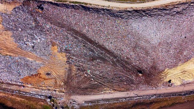 Elevated view of trash mound with heavy machinery. Aerial drone shot showing compacted waste, tire tracks and two bulldozers working the site.