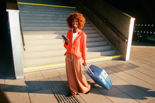 Woman portrait pulling a blue suitcase beside a stairway film photo