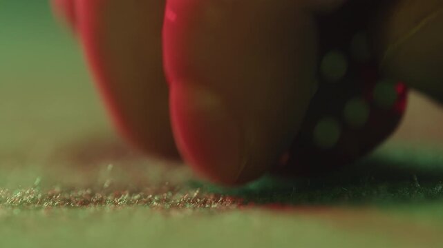 Close up of a player hand throwing two red dice on a green felt casino table during a game of craps, gambling and betting concept with luck and chance.