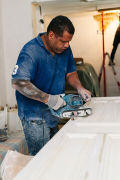 Woodworker sanding door with power tool