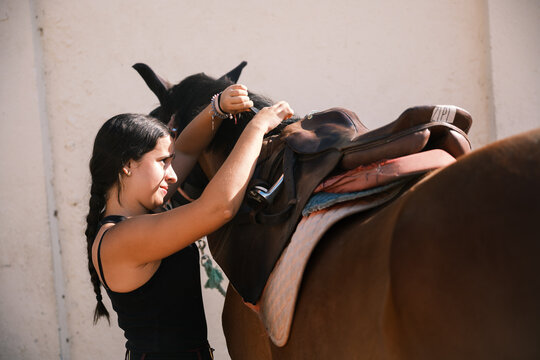 Horsewoman putting the saddle on the horse