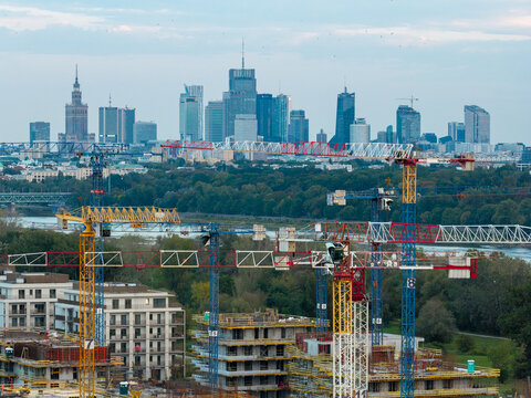 Poland - 09 September 2026: Aerial view of a construction site with multiple tower cranes, with the modern Warsaw skyline in the background, featuring glass skyscrapers and green trees.