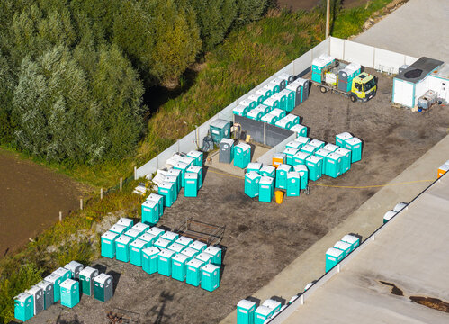 Pelplin, Pomeranian Voivodeshi, Poland - 06 September 2026: Aerial view of a large collection of portable toilets stored in a fenced yard with a service truck.