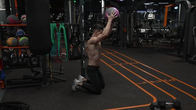 Sportsman has ball workout in fitness gym. Athlete throw fitness ball on gym floor. Fit man do ball workout in fitness gym. Fitness workout of sportsman with ball in gym. Slam training drill
