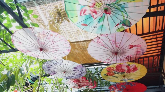Hanging decorative asian oil paper parasols with various floral and bird patterns forming an artistic ceiling installation, offering cultural ambiance and shade in an outdoor dining area