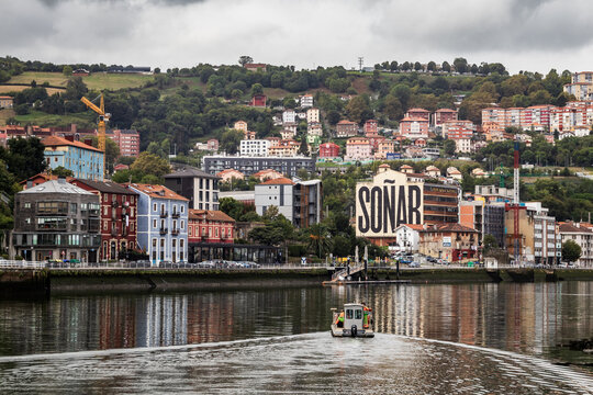 Bilbao, Pais Vasco, Espa&ntilde;a. 2 de Septiembre 2026. Vista desde la R&iacute;a de Bilbao de un barco navegando frente al ic&oacute;nico mural So&ntilde;ar en el barrio de Olabeaga con colinas de fondo.