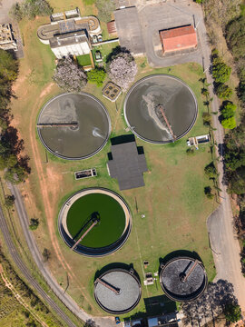 Brazil - 03 September 2026: Aerial view of a wastewater treatment plant featuring circular sedimentation tanks, industrial buildings, and surrounding green vegetation.