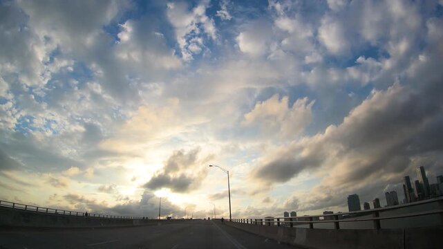 Driving through Miami at sunset under a dramatic sky, with towering clouds and warm evening light creating an atmospheric view of the city and South Florida landscape.