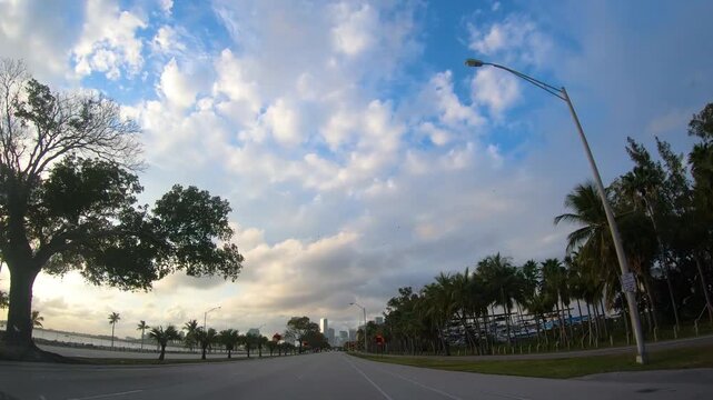 Driving POV on a Florida freeway toward Miami at sunset, with dramatic white clouds illuminated by warm evening light, capturing the atmosphere of an American road trip.