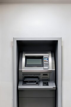 Wall-mounted ATM cash machine with blank screen and keypad in a white bank interior