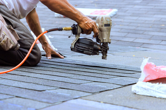 Worker installs roofing tiles using nail gun during construction project in residential area