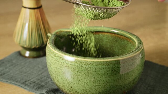Sifting bright green matcha powder using metal mesh sieve over ceramic bowl. Preparation of healthy antioxidant superfood drink for iced matcha or latte.
