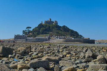 A clear day reveals St Michael's Mount castle on an island, surrounded by a vast rocky low-tide beach and a blue sky - St Michael's Mount, Cornwall, UK © Robert