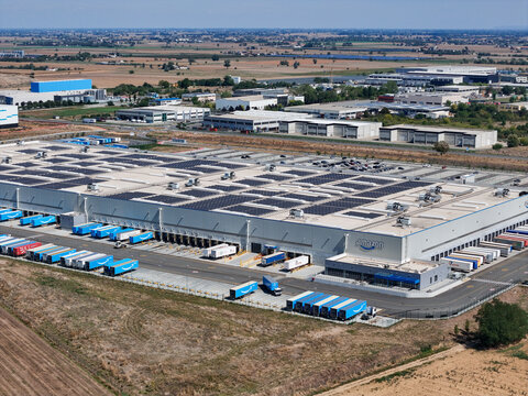 Spinetta Marengo, Piedmont, Italy - 05 September 2026: Aerial view of Amazon distribution centre featuring rooftop solar panels, blue delivery trucks at loading bays, and industrial surroundings.