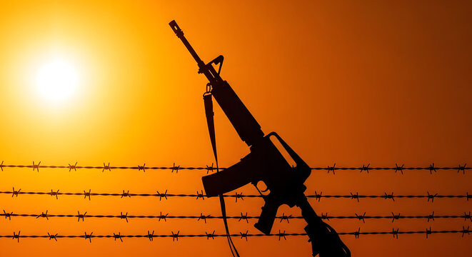 Silhouette of assault rifle against barbed wire fence at golden sunset