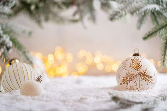 A Christmas background featuring an elegant white bauble etched with a golden diamond pattern beneath frosted pine on snow, softly lit by warm twinkling lights with generous copy space.