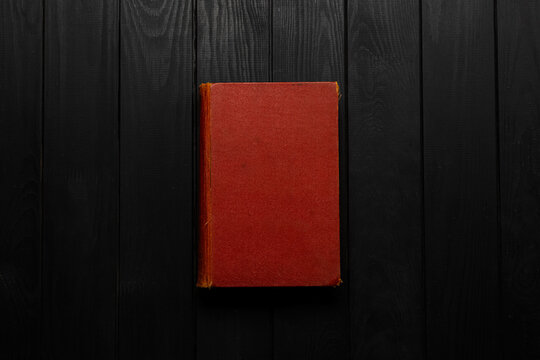 Old closed book with red hard cover on dark wooden back