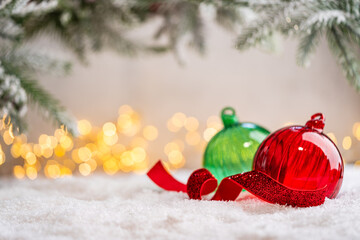 Naklejka premium A Christmas background featuring glossy transparent red and green glass baubles beside a plaid ornament beneath frosted pine on snow, softly lit by warm twinkling lights with copy space.