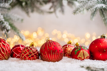 Naklejka premium A Christmas background featuring a row of red baubles with varied gold glitter patterns, bells, and holly beneath frosted pine on snow, softly lit by warm twinkling lights with copy space.