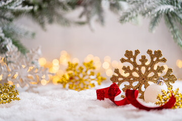 Naklejka premium A Christmas background featuring large golden and white glittering snowflakes beside a red ribbon and white bauble beneath frosted pine on snow, softly lit by warm twinkling lights with copy space.