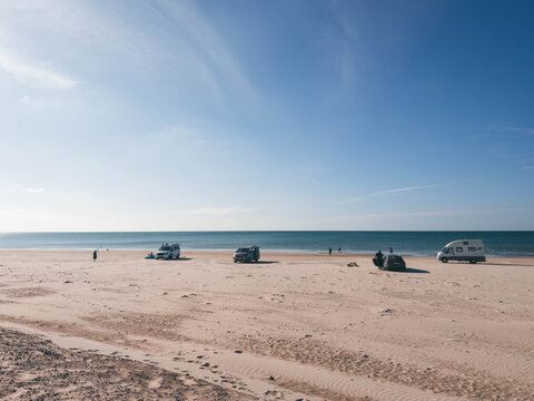 Cars driving and parked on wide sandy beach under bright sunny blue sky, Denmark