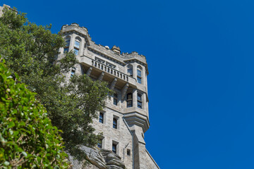 Upward view of a historic stone castle or monastery with turrets and a balcony, framed by green foliage - St Michael's Mount, Cornwall, UK © Robert