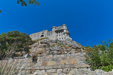 A majestic stone castle crowns a rocky hill against a clear blue sky, with lush greenery at its base - St Michael's Mount, Cornwall, UK © Robert