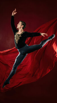 Ballet dancer performing a dynamic jump against flowing red fabric, wearing a black and gold patterned top and dark fitted tights.