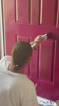 Handyman painting lower portion of the front door of a house red