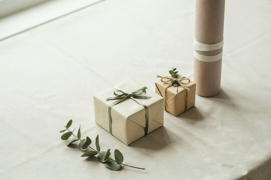 Two neutral colored gift boxes wrapped in simple paper with string and eucalyptus leaves