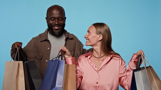 Portrait of smiling young African American man and Caucasian woman holding shopping bags. Clip suitable for retail advertising, holiday sales promotions, discount marketing, consumer campaigns