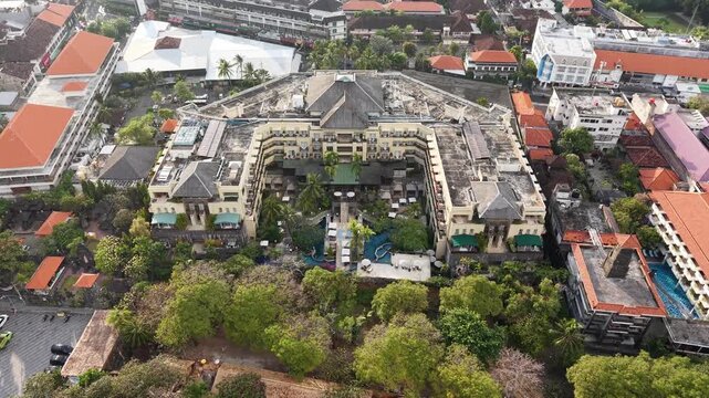 Aerial photo of a Seminyak, Bali hotel resort with central pool, lush tropical gardens and surrounding urban rooftops, conveying travel, vacation and island hospitality in a busy coastal town