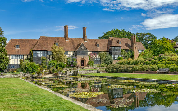 Historisches Tudor-inspiriertes Herrenhaus im RHS Garden Wisley mit gepflegten G&auml;rten, Seerosenteich und sommerlichem blauen Himmel in Surrey, England.