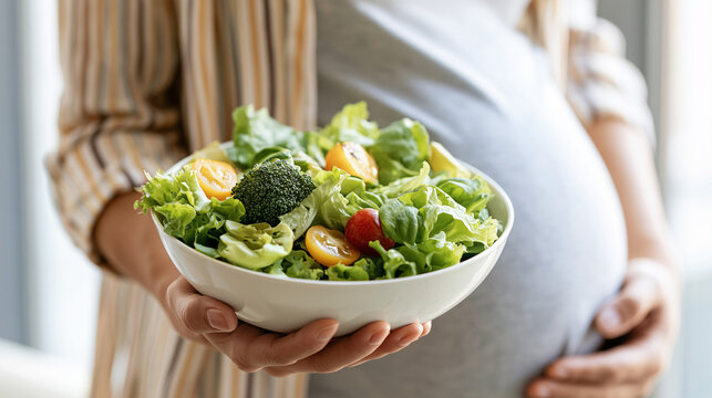 Close up of a pregnant woman holding a bowl of fresh green salad with broccoli and cherry tomatoes.