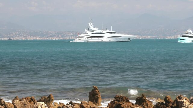 Luxury yachts cruising off the coast of Antibes on the French Riviera with Mediterranean Sea and Alps in background, France