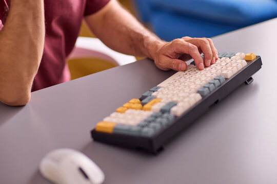 Close-up view of right-handed adult forearm and hand typing on compact mechanical keyboard with colorful keycaps on gray office desk under soft studio lighting