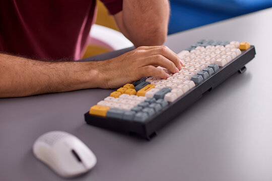 Close-up view of right-handed adult forearm and hand typing on compact mechanical keyboard with colorful keycaps on gray office desk under soft studio lighting