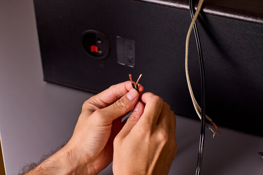 Two hands holding stripped copper wire ends beside electronic enclosure during wiring repair, warm studio lighting with closeup detail of exposed conductor strands