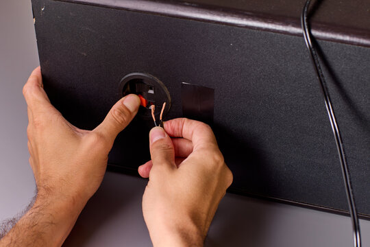 Two hands holding stripped copper wire ends beside electronic enclosure during wiring repair, warm studio lighting with closeup detail of exposed conductor strands