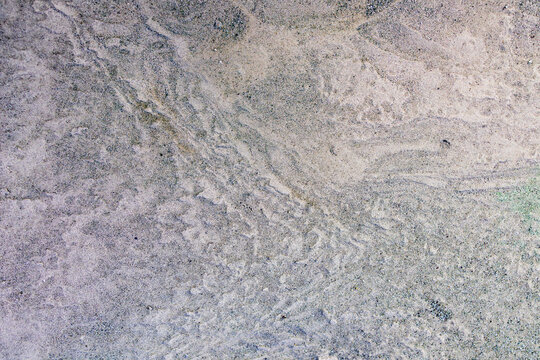High res texture of wet beach sand showing intricate tidal wave ripples and fine grains, a smooth sandy shoreline surface with natural water flow patterns