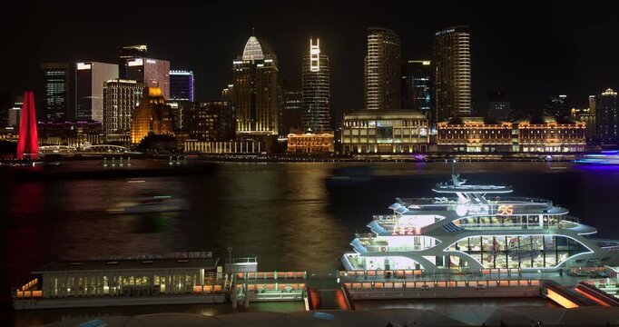 SHANGHAI, CHINA - AUGUST 23, 2026: Cruise boats dock and depart at illuminated river wharf with Bund skyline across Huangpu River at night in SHANGHAI CHINA, in timelapse