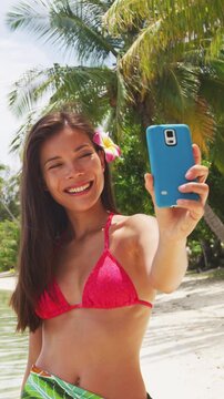 Woman taking smart phone selfie video or photo- Bikini travel girl on beach smiling happy on Matira Beach, Bora Bora. Joyful girl on holidays beach vacation wearing bikini in Tahiti, French Polynesia.