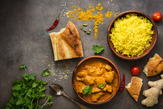 Chicken tikka masala in a bowl with basmati rice and naan bread on a dark rustic background, top view, flat lay. Traditional spicy Indian dish.