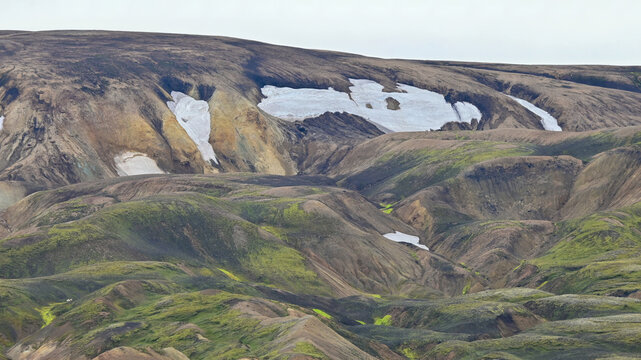 Vibrant colorful mountains with lingering snow and moss-covered slopes in Landmannalaugar, Icelandic highlands, viewed from above.